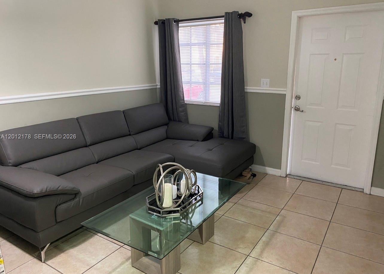 A living room features a gray sectional sofa, a glass coffee table, and tile flooring — 6995 NW 173rd Dr # 2105, Hialeah FL 33015, HIALEAH, FL
