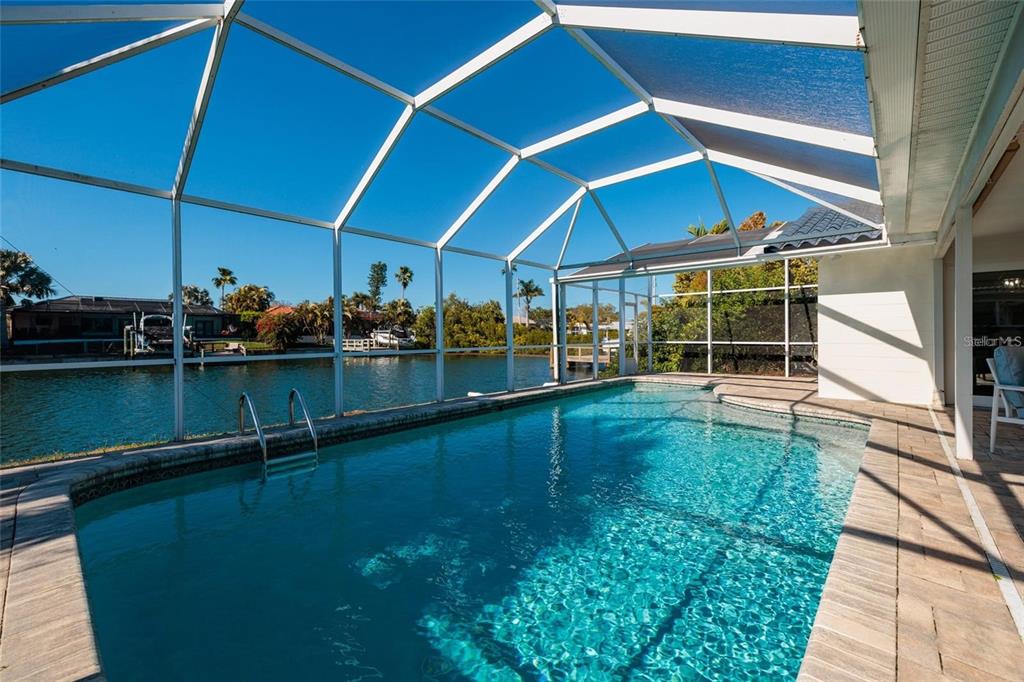 A screened-in swimming pool overlooks a canal with neighboring houses in the background — 1985 MICHIGAN AVENUE NE, ST PETERSBURG, FL