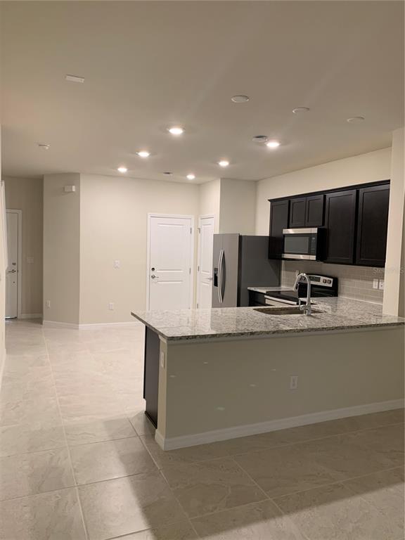 A kitchen features dark wood cabinets, granite countertops, a stainless steel refrigerator, and tile flooring — 2567 BUENA VIEW ROAD, KISSIMMEE, FL
