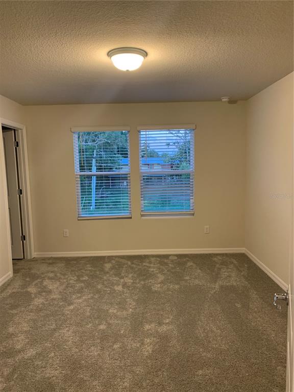 An empty bedroom features beige walls, gray carpeting, a ceiling light, and two windows — 2567 BUENA VIEW ROAD, KISSIMMEE, FL