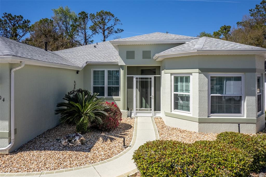 A light-colored single-story house exterior features a front entrance with a screen door and landscaping — 15304 SW 15TH TERRACE ROAD, OCALA, FL