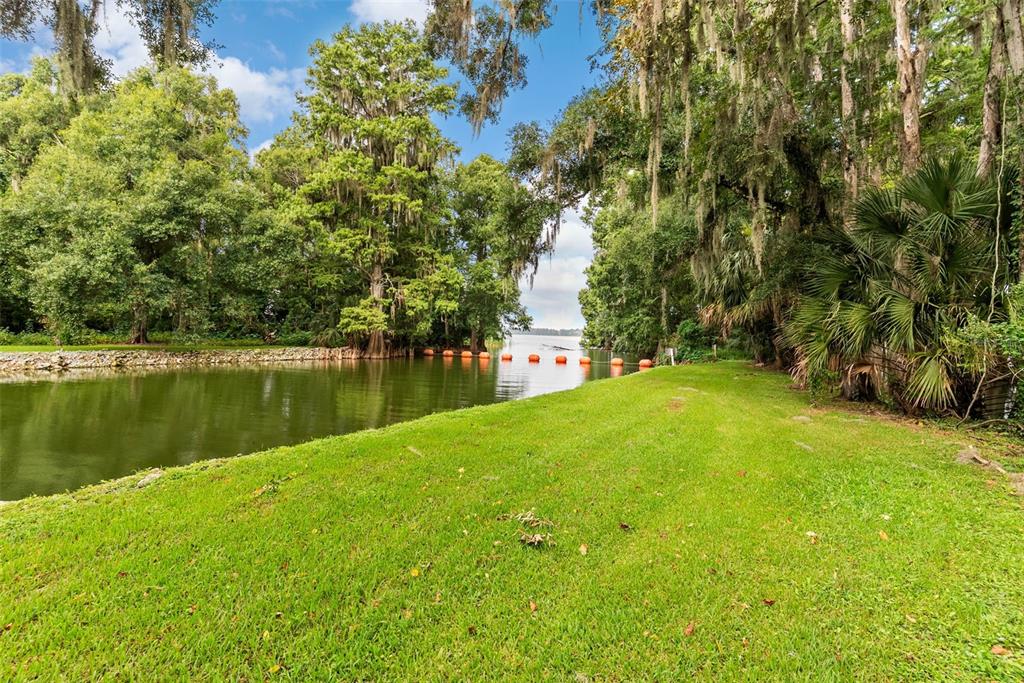 A grassy lawn leads to a narrow canal lined with trees and orange floating buoys — 12311 KELSO ROAD, THONOTOSASSA, FL