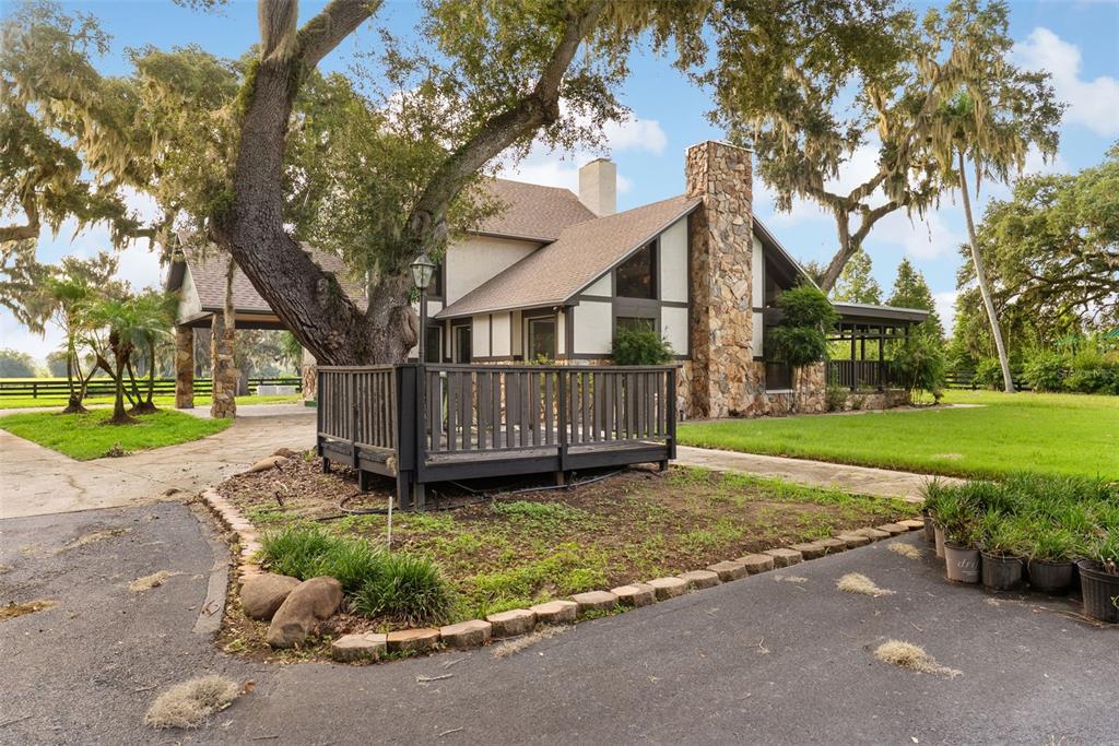 A two-story house with a stone chimney, a wooden deck, and large oak trees — 12311 KELSO ROAD, THONOTOSASSA, FL