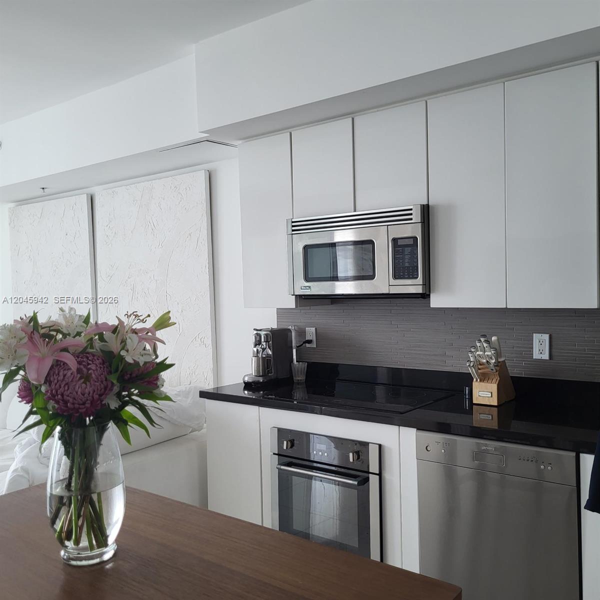 A modern kitchen features white cabinets, black countertops, stainless steel appliances, and a gray backsplash — 92 SW 3rd St # 3207, Miami FL 33130, MIAMI, FL