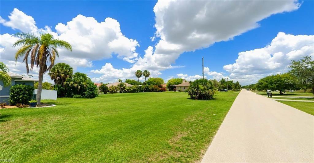 A large, grassy vacant lot is situated next to a paved road and palm trees — 1825 SW 47TH TERRACE, CAPE CORAL, FL