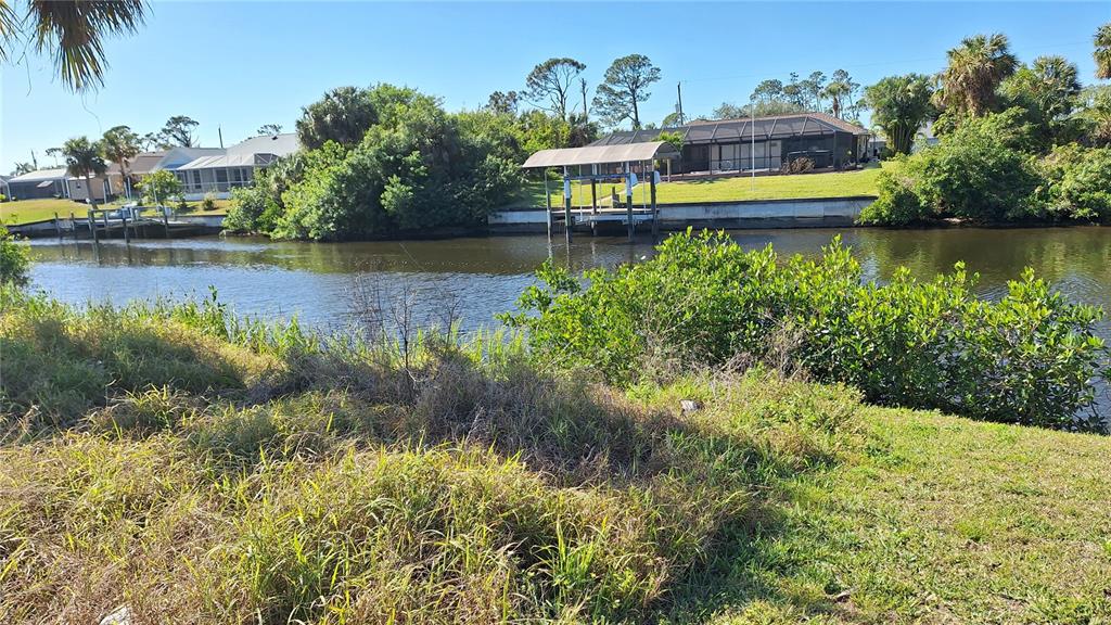 A canal view features a boat dock, lush vegetation, and houses in the background — 3173 ROCK CREEK DRIVE, PORT CHARLOTTE, FL