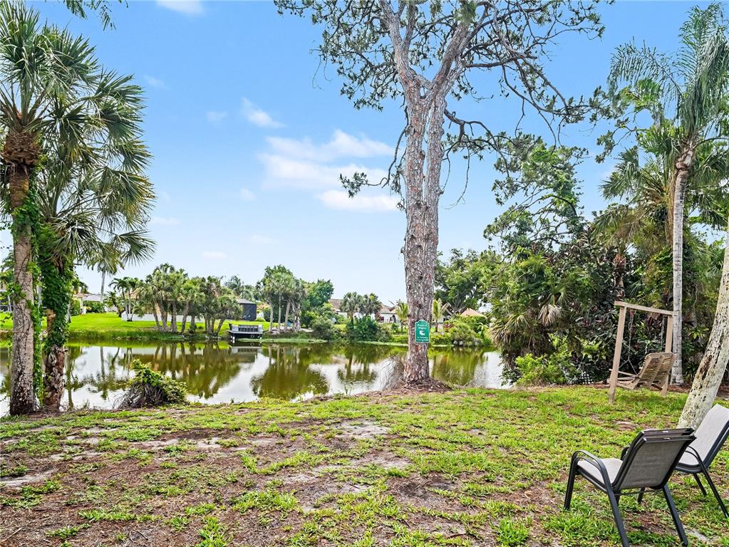 A grassy backyard overlooks a small pond with palm trees and a wooden swing — 2320 LAKE SHORE DRIVE, NOKOMIS, FL