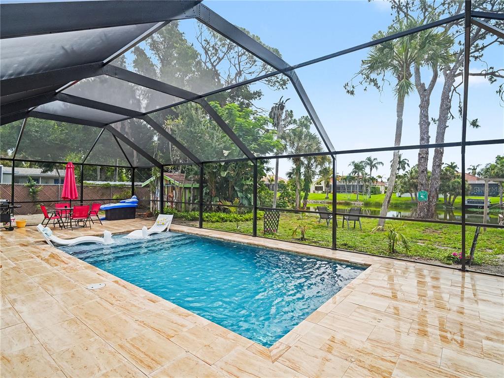 A screened-in pool patio features light-colored stone tiles, lounge chairs, and a view of water — 2320 LAKE SHORE DRIVE, NOKOMIS, FL