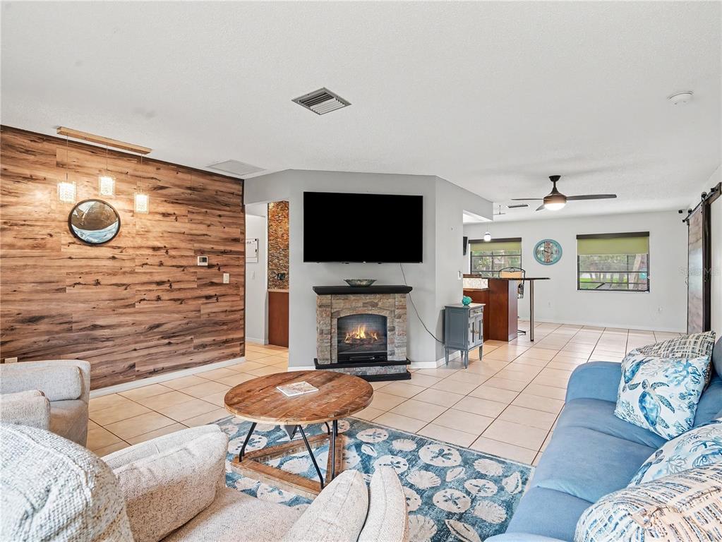A living room features a stone fireplace, a wall with wood paneling, and tile flooring — 2320 LAKE SHORE DRIVE, NOKOMIS, FL