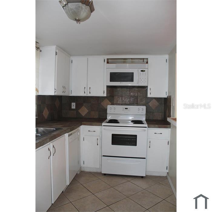 A kitchen with white cabinets, white appliances, dark tile backsplash, and diagonal floor tiles — 8605 CHAMPLAIN COURT UNIT 84, TAMPA, FL