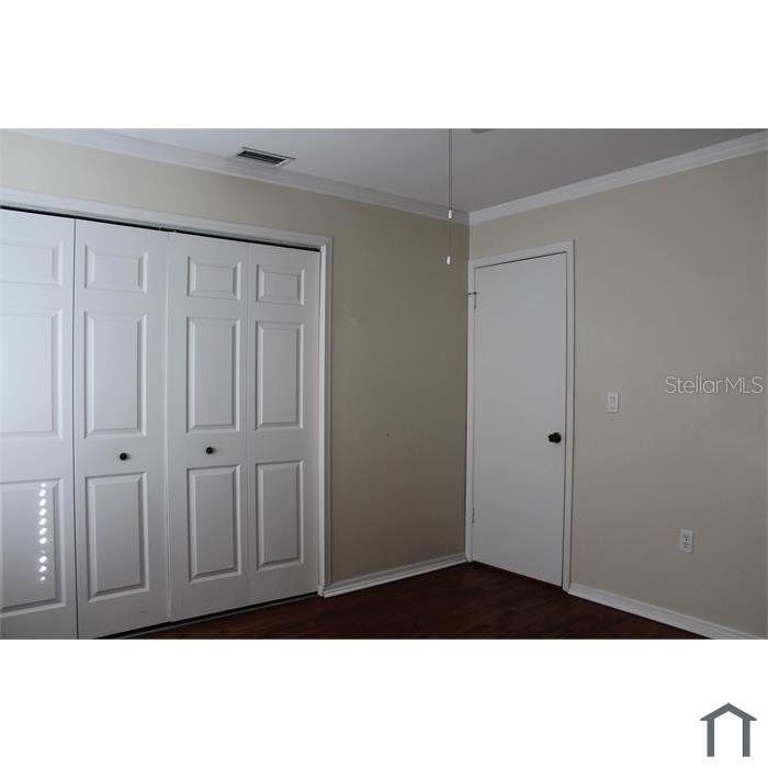A bedroom features white paneled closet doors, a single interior door, and dark wood flooring — 8605 CHAMPLAIN COURT UNIT 84, TAMPA, FL
