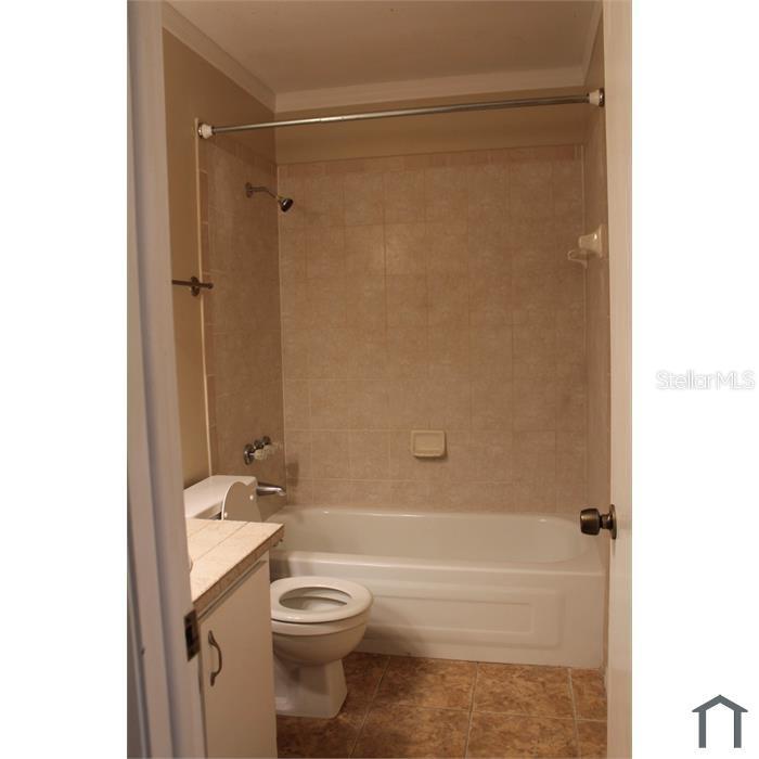 A bathroom featuring a beige tiled shower-tub combo, a white toilet, and light-colored cabinetry — 8605 CHAMPLAIN COURT UNIT 84, TAMPA, FL