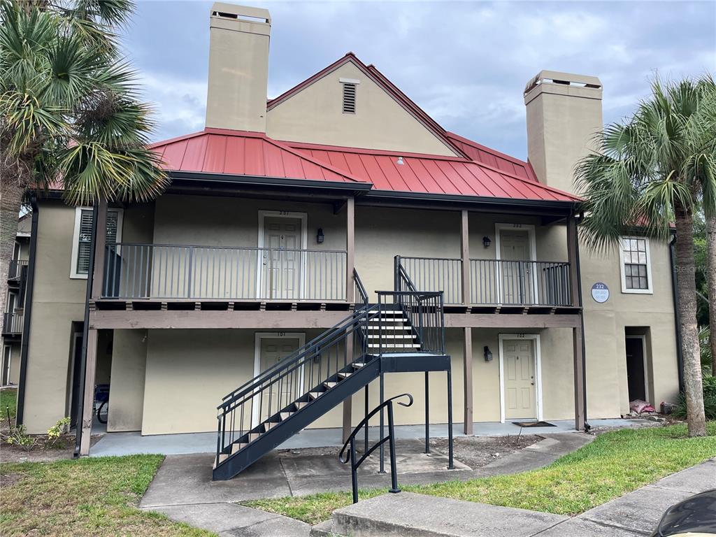 A two-story apartment building features a red metal roof, tan stucco walls, and exterior stairs — 232 AFTON SQUARE UNIT 201, ALTAMONTE SPRINGS, FL