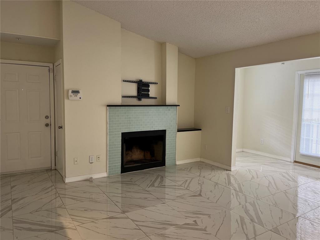 A living room features a fireplace with light blue tile, marble-look flooring, and white walls — 232 AFTON SQUARE UNIT 201, ALTAMONTE SPRINGS, FL
