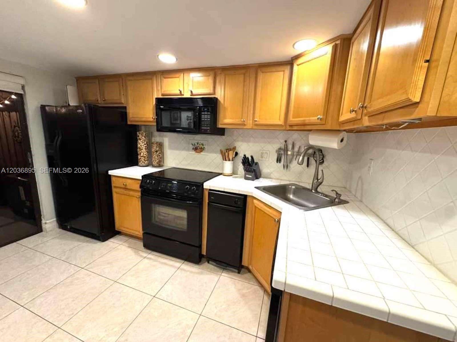A kitchen features light wood cabinets, black appliances, and white tiled countertops and floors — 10044 SW 77th Ct # 0, Miami FL 33156, MIAMI, FL
