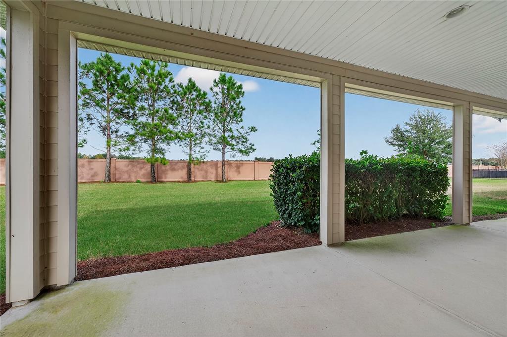A covered concrete patio overlooks a grassy backyard enclosed by a tall tan wall — 3947 NW 46TH TERRACE, OCALA, FL