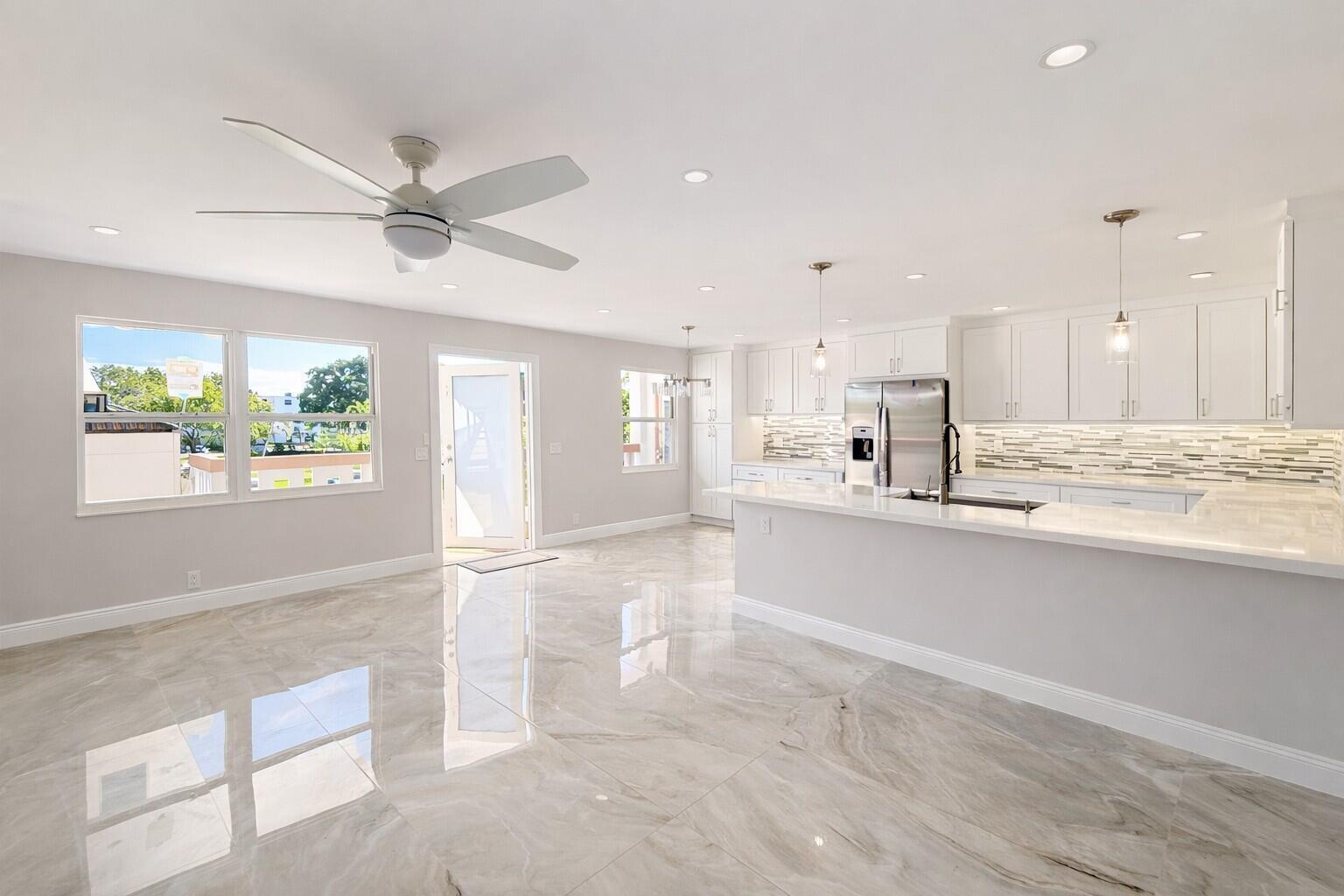 A bright, open-concept kitchen and living area featuring white cabinetry, quartz countertops, and marble-look flooring — 2019 Wolverton A, Boca Raton FL 33434, BOCA RATON, FL