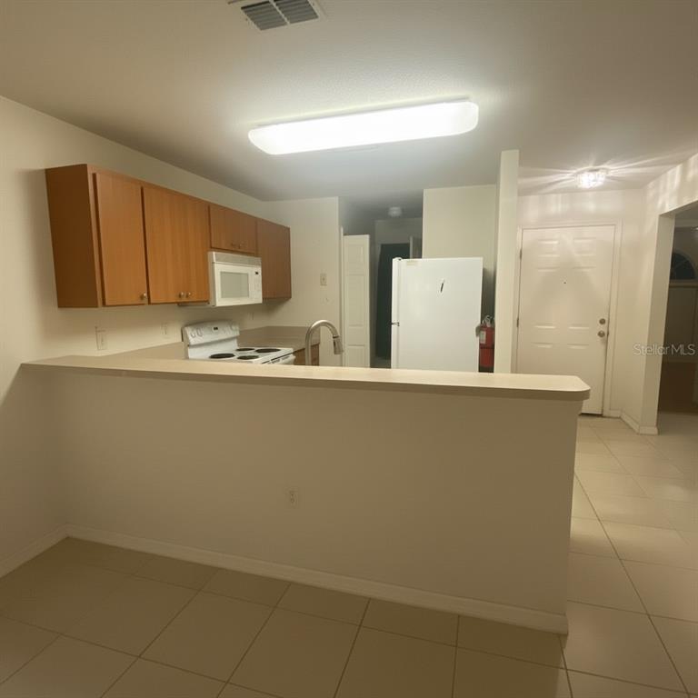 A kitchen with light-colored tile flooring, wood cabinets, white appliances, and a breakfast bar — 2150 MYSTIC RING LOOP, KISSIMMEE, FL