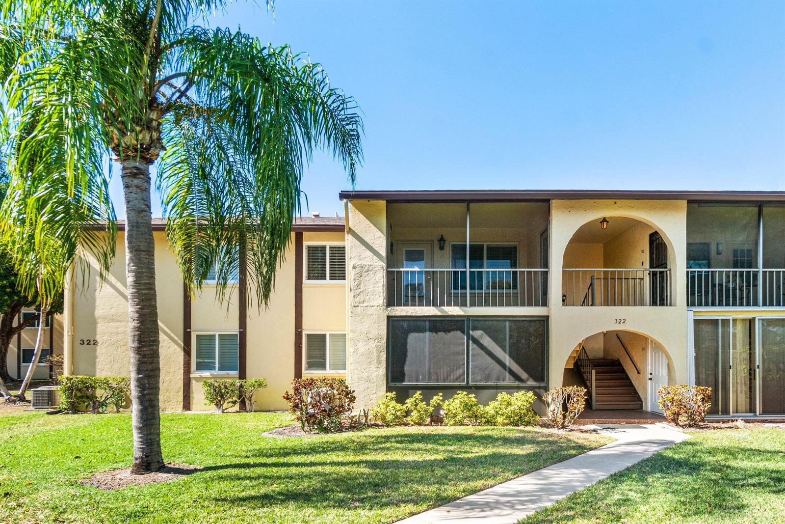 A two-story apartment building features a palm tree, screened balconies, and an arched entryway — 322 Pine Ridge Circle # 2, FL 33463, FL