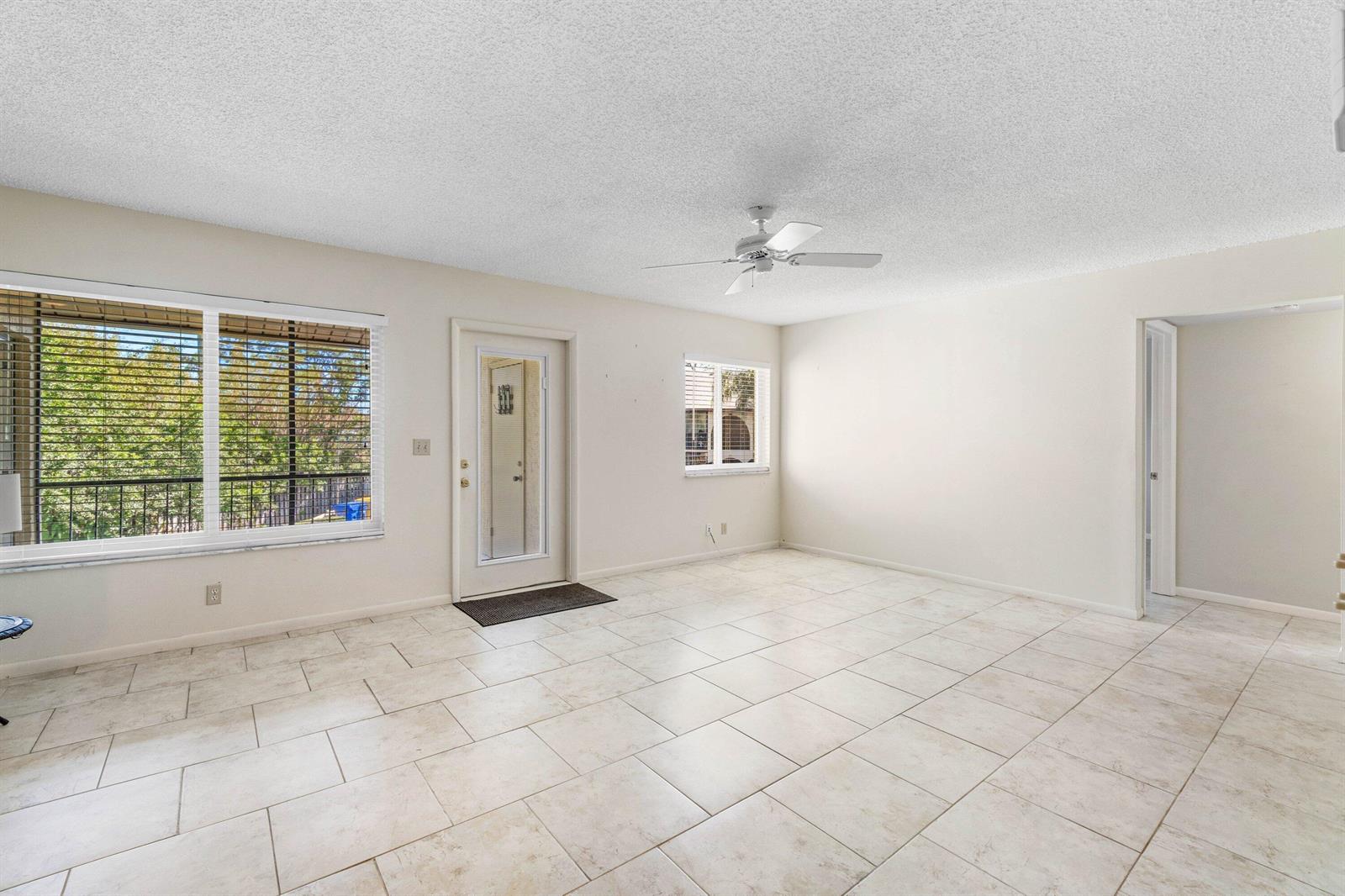 An empty room features white walls, light-colored tile flooring, a ceiling fan, and a glass door — 322 Pine Ridge Circle # 2, FL 33463, FL