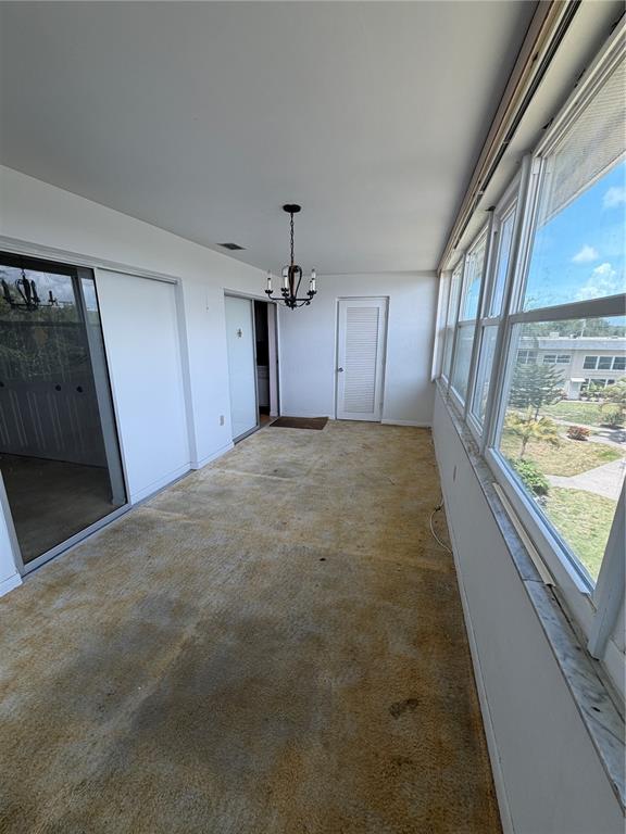 An enclosed sunroom features a worn carpet, a chandelier, and large windows overlooking a lawn — 5725 12TH AVENUE N UNIT 306D, ST PETERSBURG, FL