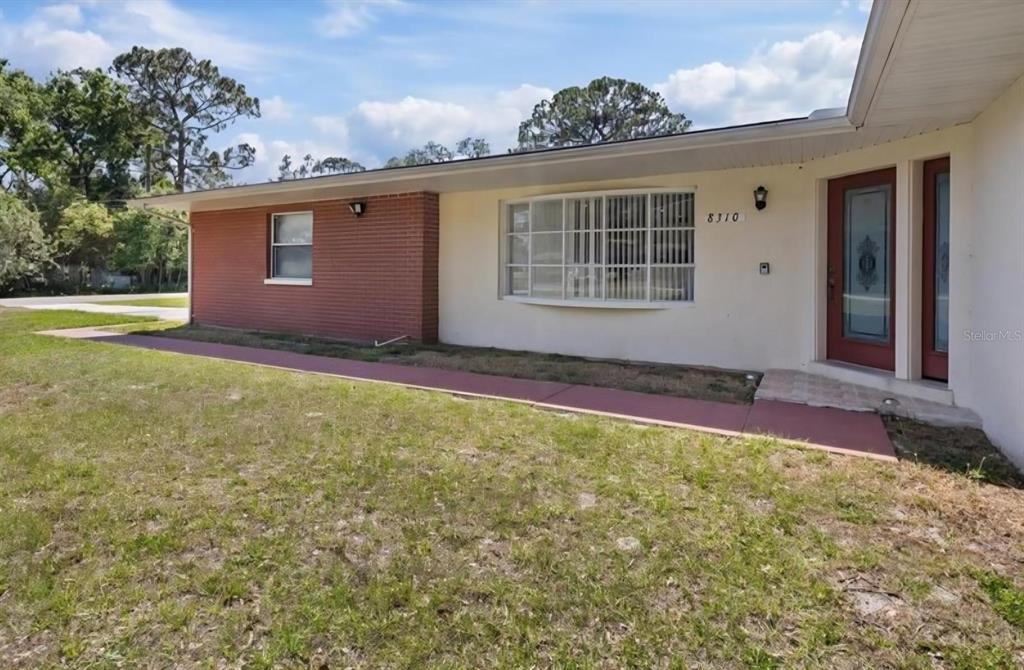 A single-story house exterior features a red brick section, a bay window, and a red door — 8310 PAT BOULEVARD, TAMPA, FL