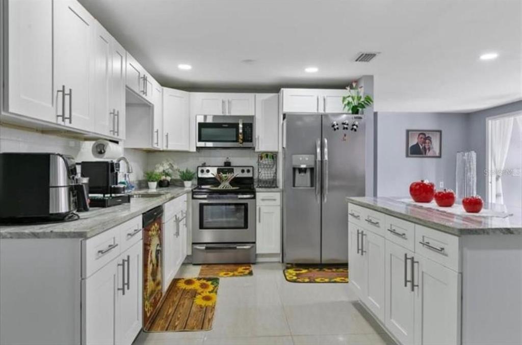 A kitchen features white cabinetry, stainless steel appliances, and a central island with granite countertops — 8310 PAT BOULEVARD, TAMPA, FL