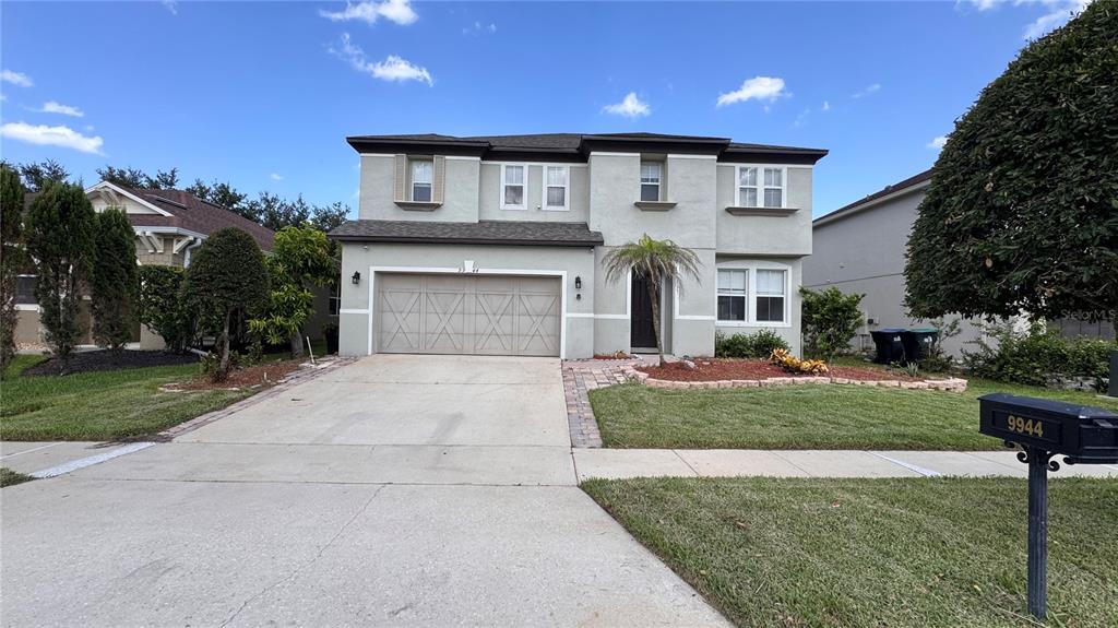 A two-story suburban house with a beige stucco exterior, a two-car garage, and a lawn — 9944 CHORLTON CIRCLE, ORLANDO, FL