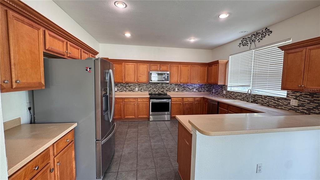 A kitchen features wood cabinets, stainless steel appliances, a tile floor, and a breakfast bar — 9944 CHORLTON CIRCLE, ORLANDO, FL