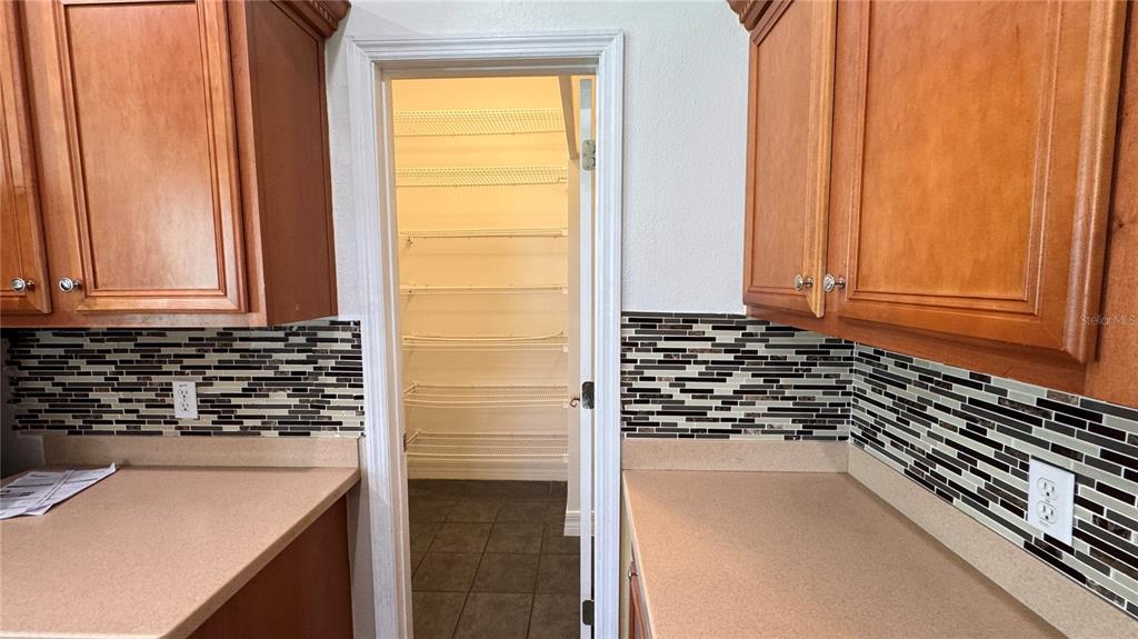 A kitchen features wood cabinets, a beige countertop, a tiled backsplash, and an open pantry — 9944 CHORLTON CIRCLE, ORLANDO, FL