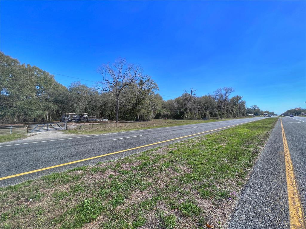 A paved road runs alongside a grassy area with a metal gate and wooded land — 14621 NW HIGHWAY 19, CHIEFLAND, FL