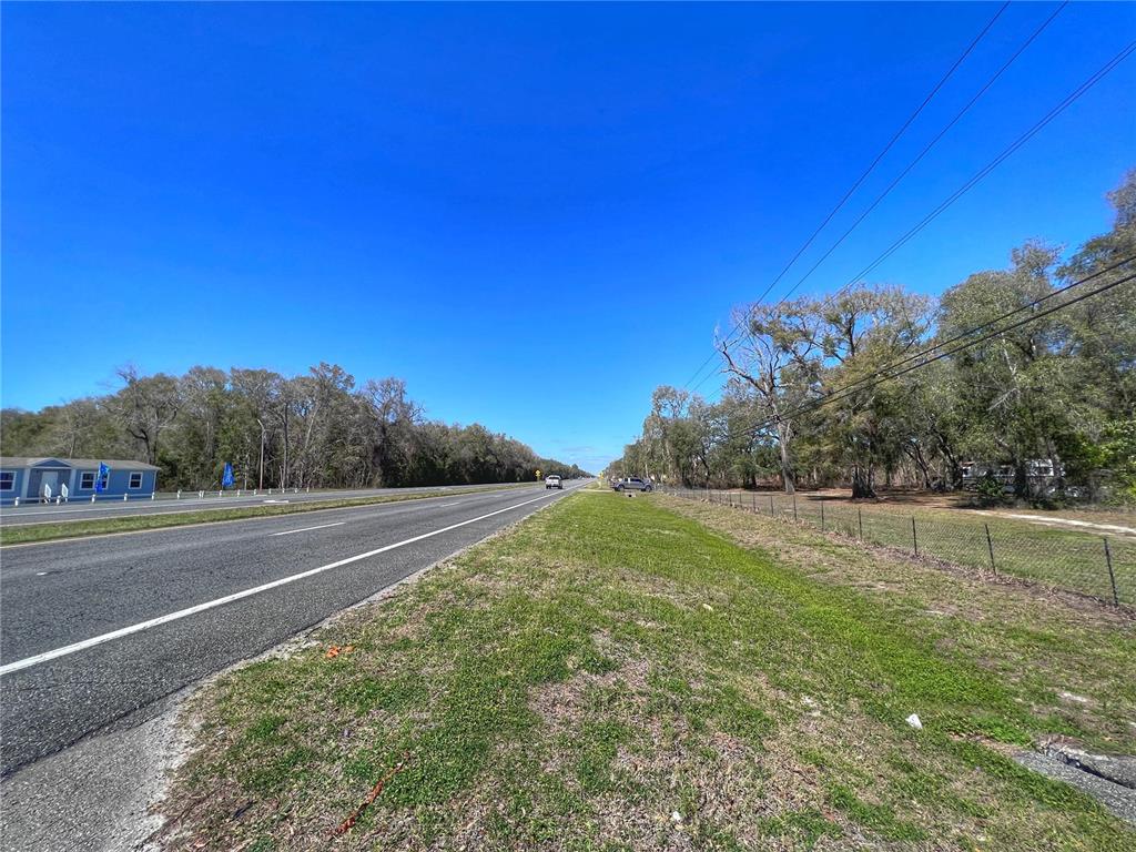 A paved road runs alongside a grassy shoulder with trees and a chain-link fence — 14621 NW HIGHWAY 19, CHIEFLAND, FL