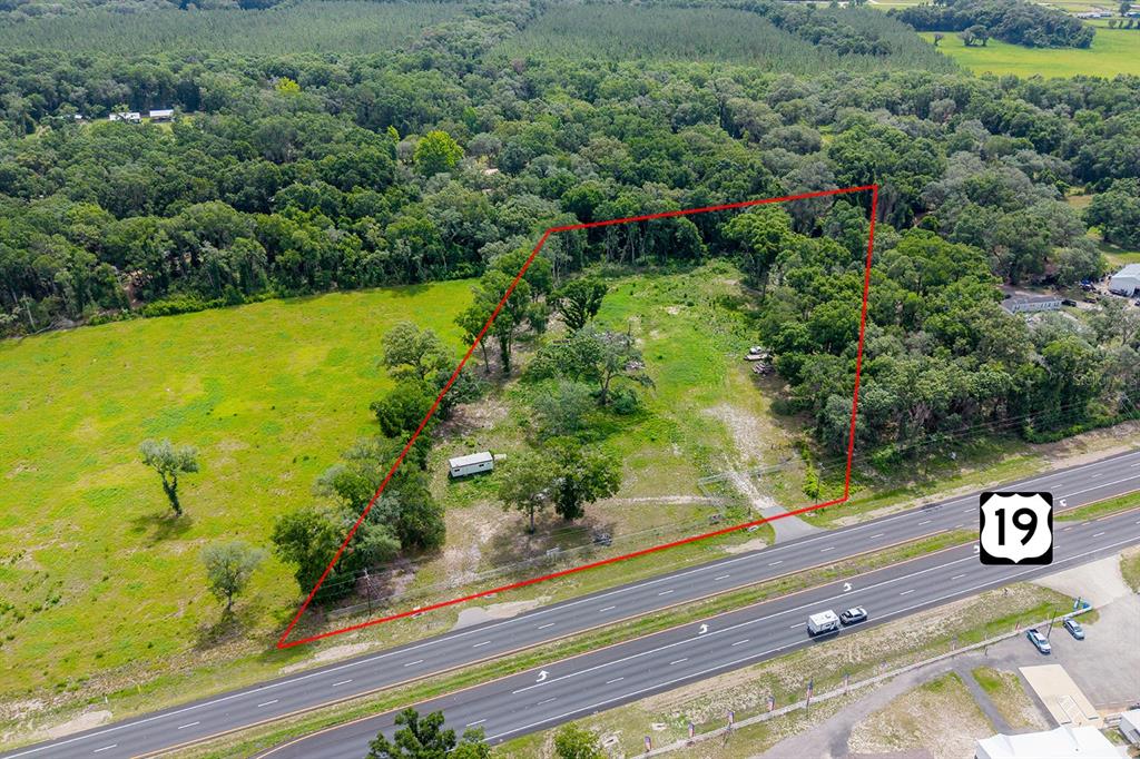 An aerial view shows a vacant, grassy lot bordered by trees and a highway — 14621 NW HIGHWAY 19, CHIEFLAND, FL