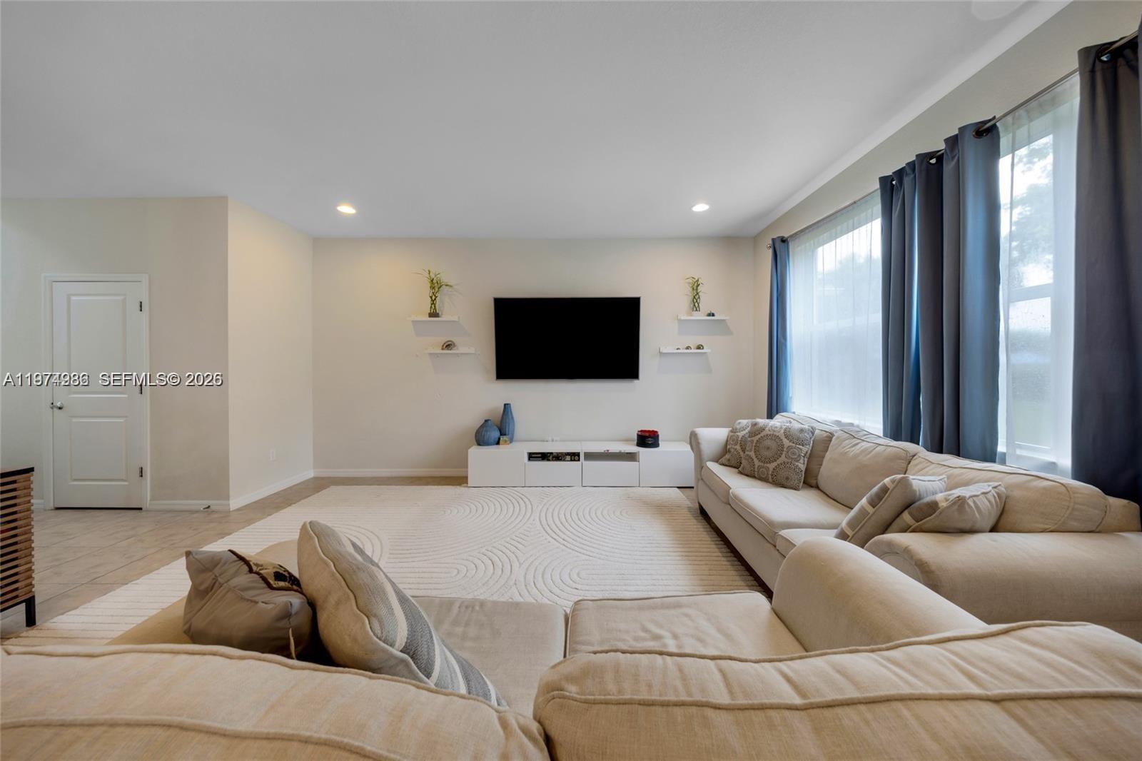 A living room features a wall-mounted television, white media console, and a large sectional sofa — 932 Banyan Dr, Hollywood FL 33021, HOLLYWOOD, FL