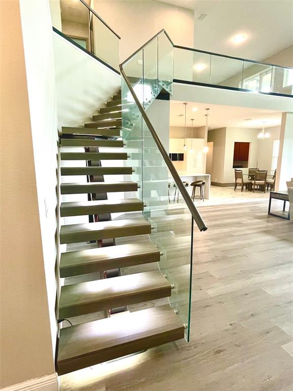 A modern staircase with wooden treads and glass railings leads to an upper level — 7759 GREEN MOUNTAIN WAY, WINTER GARDEN, FL