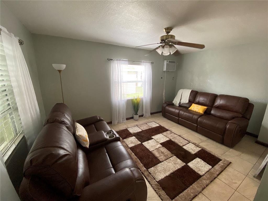 A living room features two brown leather sofas, a patterned area rug, and tile flooring — 1023 W GORE STREET W, ORLANDO, FL