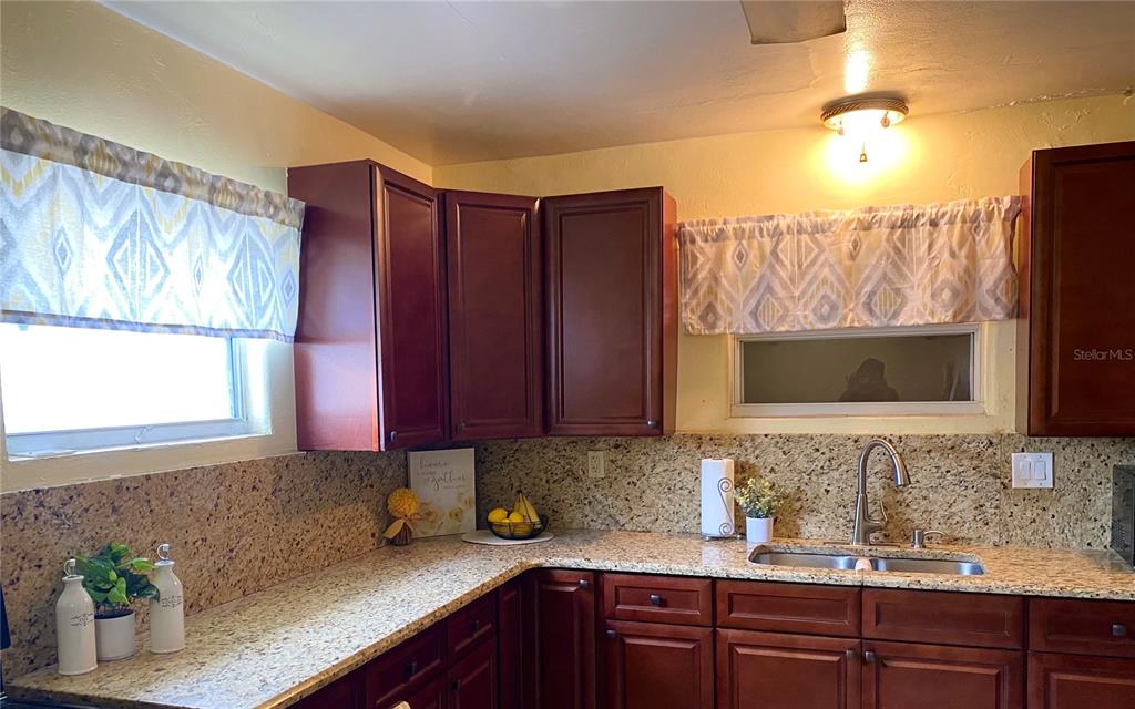 A kitchen features dark wood cabinets, granite countertops, a stainless steel sink, and patterned valances — 1023 W GORE STREET W, ORLANDO, FL