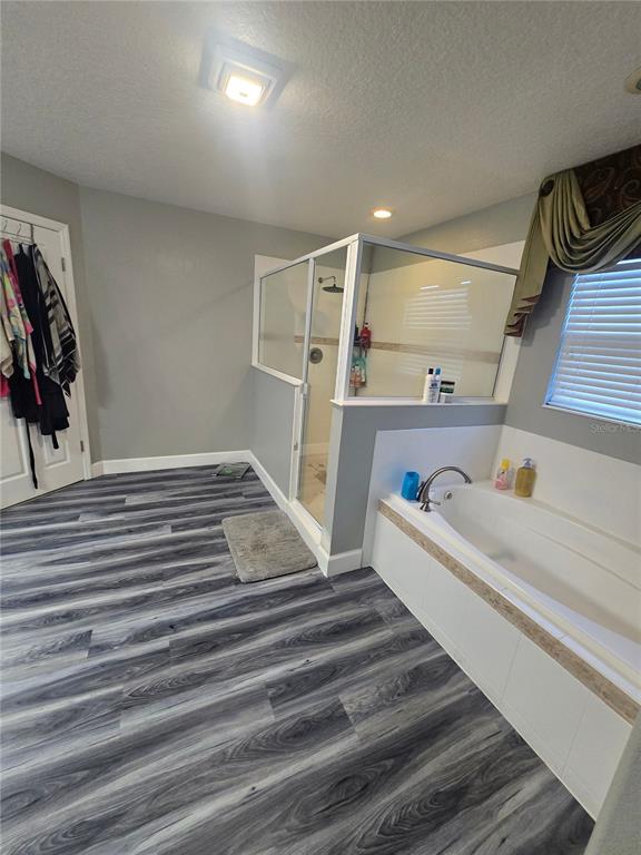 A bathroom features gray wood-look flooring, a glass-enclosed shower, and a built-in soaking tub — 510 BROOKESHIRE DRIVE, DAVENPORT, FL