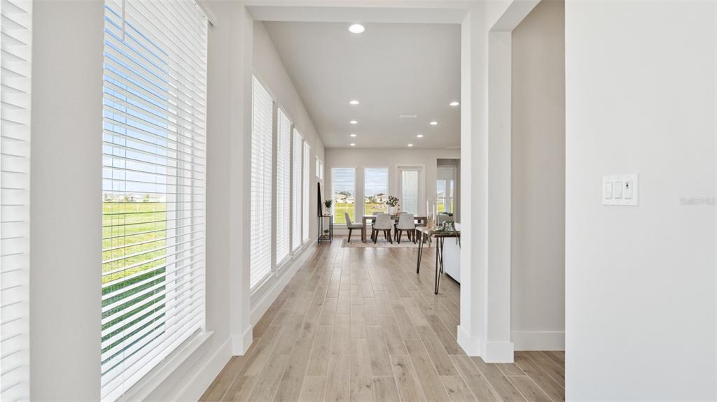 A bright hallway with wood-look tile flooring leads to a dining area with large windows — 3812 109TH STREET EAST, PALMETTO, FL