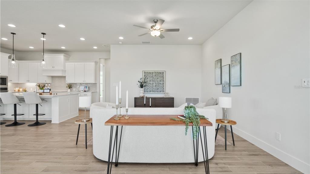 A bright, open-concept living room features a white sofa, wood console table, and adjacent kitchen — 3812 109TH STREET EAST, PALMETTO, FL