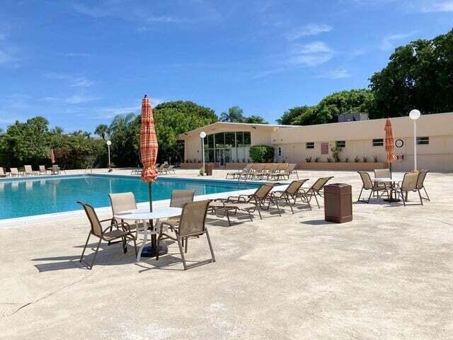 An outdoor swimming pool area features lounge chairs, tables with umbrellas, and a clubhouse building — 480 Executive Center Drive # 4a, West Palm Beach FL 33401, WEST PALM BEACH, FL