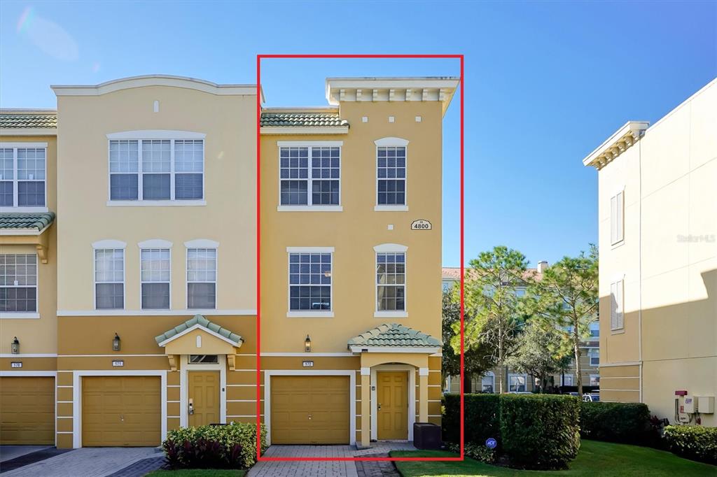 A three-story yellow townhouse with a single-car garage and a tiled entryway — 4800 TIDECREST AVENUE UNIT 172, ORLANDO, FL