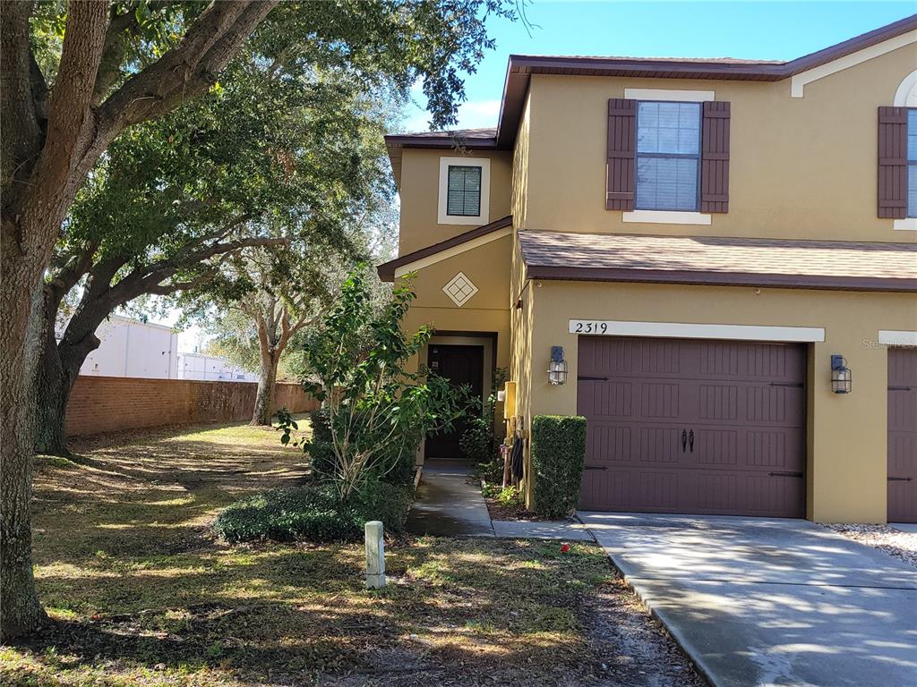 A two-story tan townhouse features a brown garage door, dark shutters, and a front walkway — 2319 ALOHA BAY COURT, OCOEE, FL