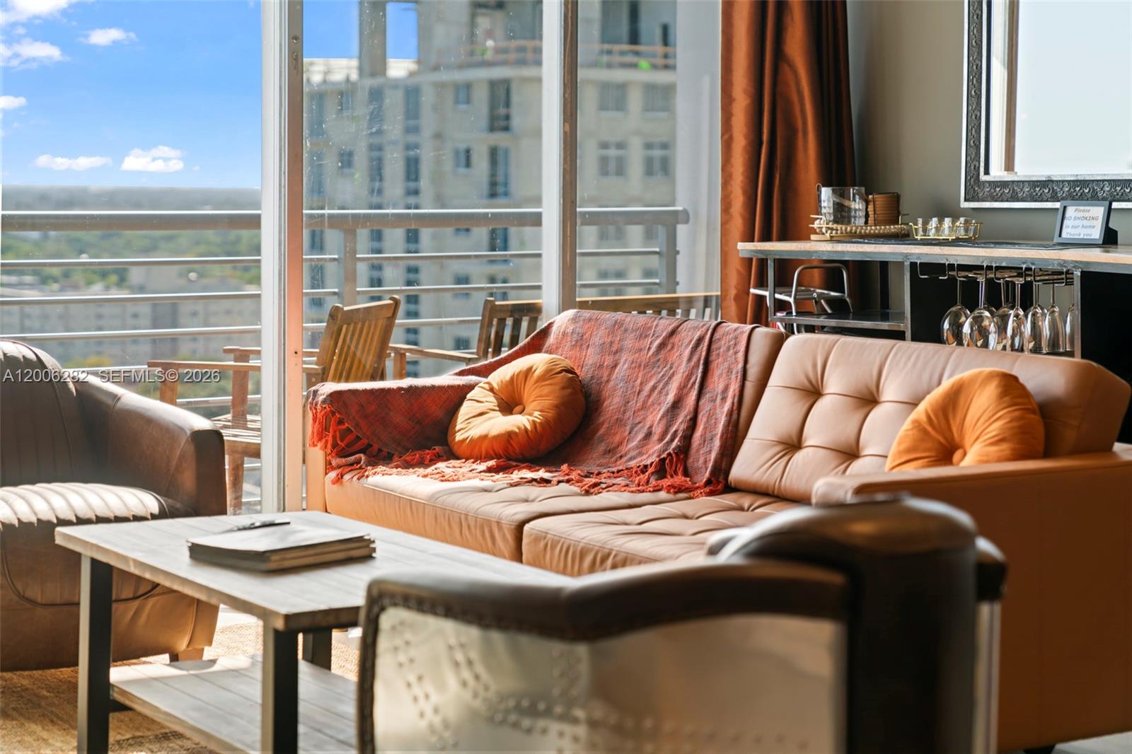 A living room features a tan leather sofa, orange pillows, and a balcony with city views — 1720 Harrison St # 1725, Hollywood FL 33020, HOLLYWOOD, FL