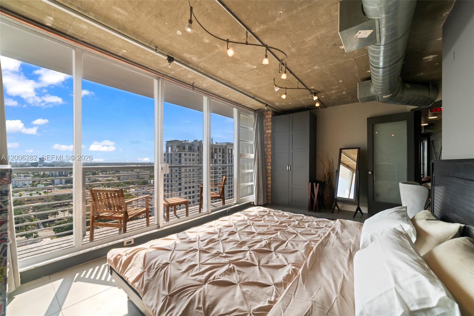 A bedroom with a concrete ceiling, track lighting, and floor-to-ceiling windows overlooking a city balcony — 1720 Harrison St # 1725, Hollywood FL 33020, HOLLYWOOD, FL