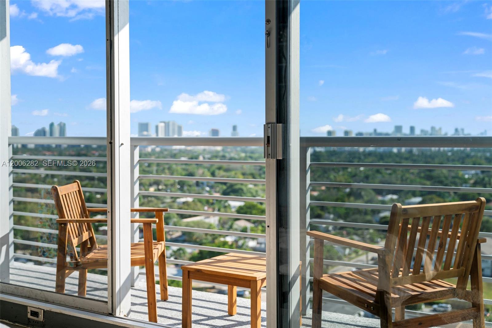 A balcony with two wooden chairs and a small table overlooks a city skyline — 1720 Harrison St # 1725, Hollywood FL 33020, HOLLYWOOD, FL