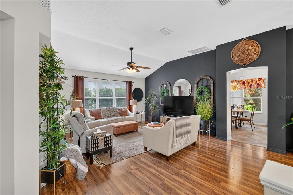 A living room features a dark accent wall, vaulted ceilings, and wood-look flooring — 313 GONZALES PLACE, LADY LAKE, FL