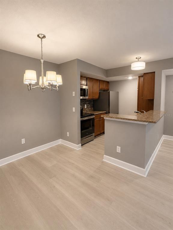 A galley kitchen features wood cabinets, granite countertops, stainless steel appliances, and light wood flooring — 5124 CONROY ROAD UNIT 17, ORLANDO, FL