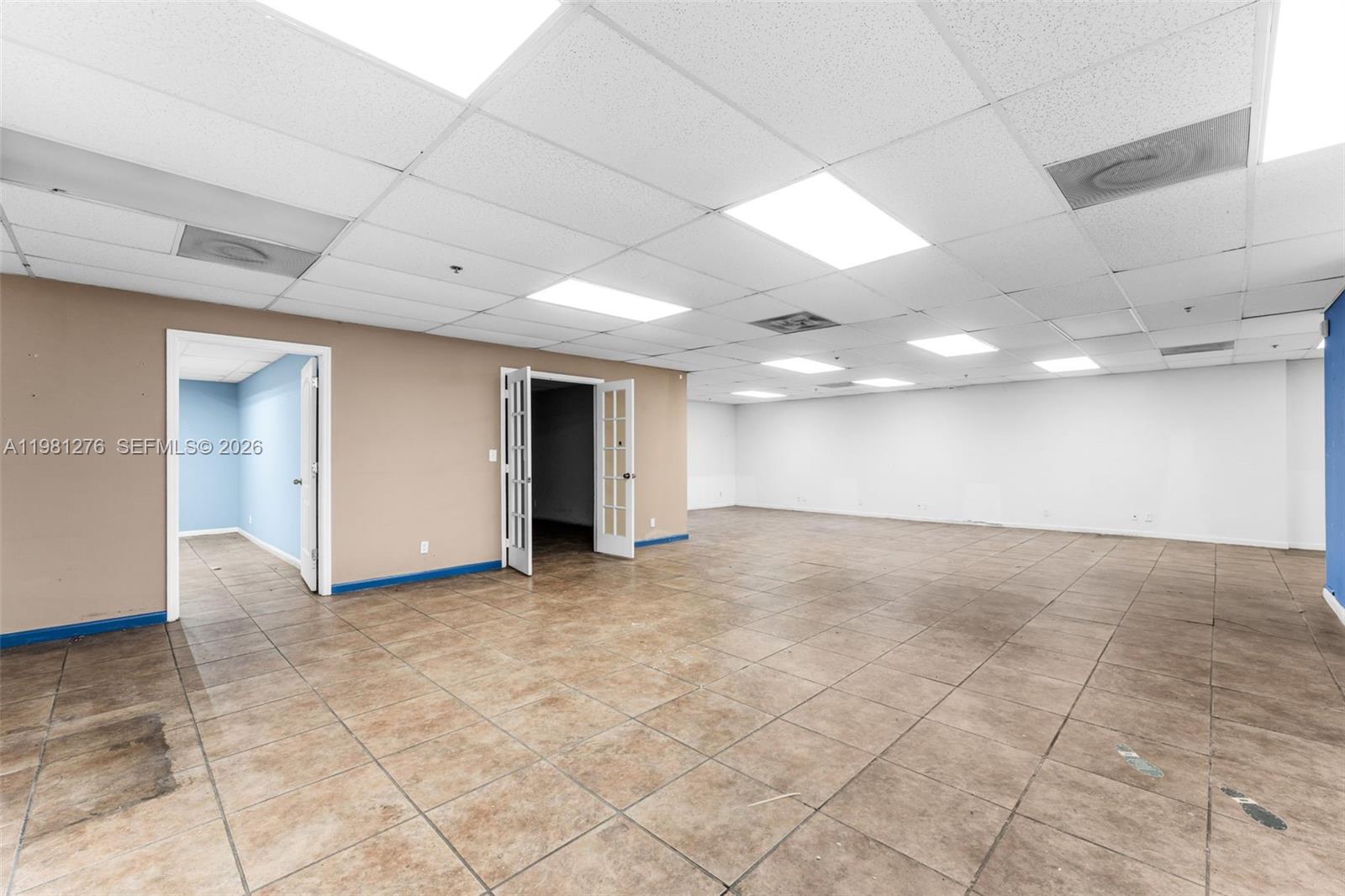 An empty office space features tan tile flooring, a drop ceiling, and two doorways — 7620 W 2nd Ct, Hialeah FL 33014, HIALEAH, FL