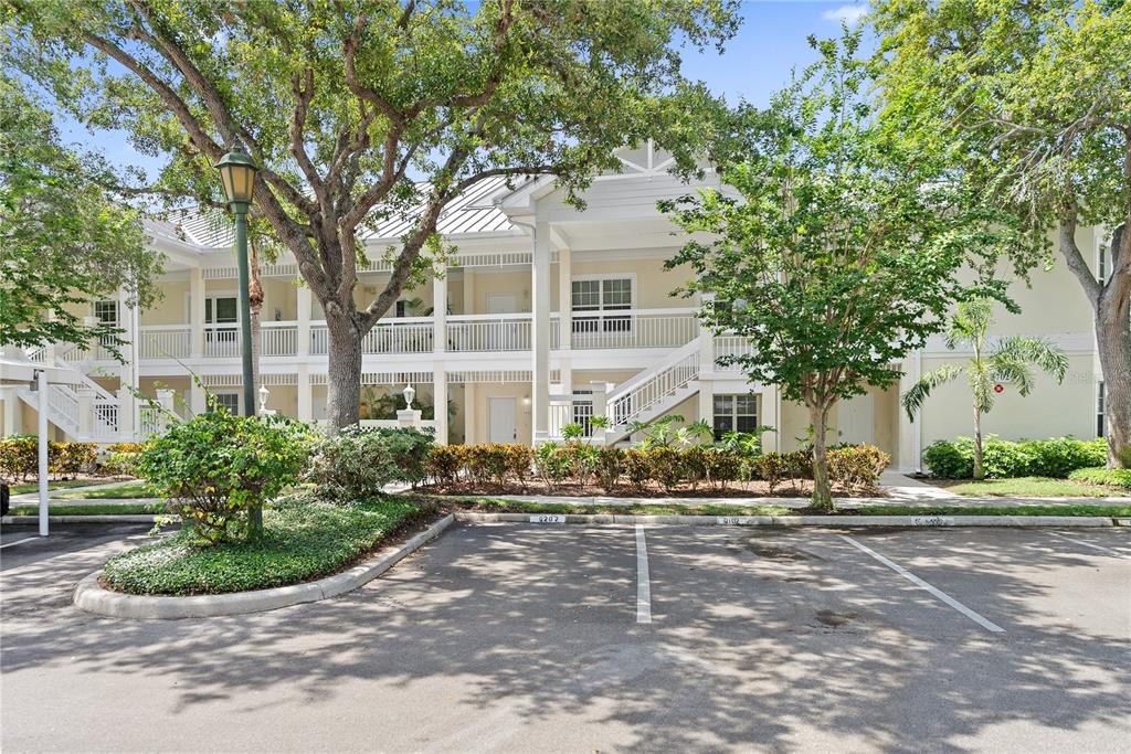 A two-story apartment building with a parking lot and mature trees in the foreground — 3702 54TH DRIVE W UNIT 102, BRADENTON, FL